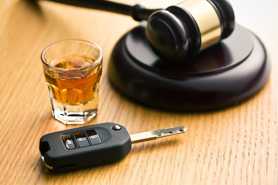 shot glass of liquor, car key, and gavel lying on wooden table