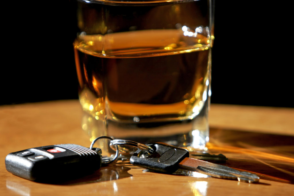 pair of car keys beside a glass of alcohol on wooden table