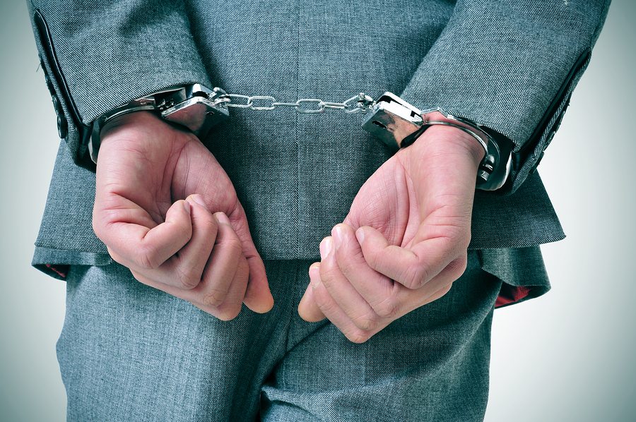 a man wearing a suit with his wrists handcuffed in the back a man wearing a suit with his wrists handcuffed in the back