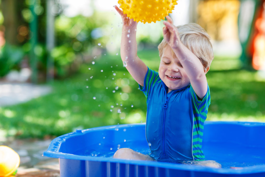 child splashing around blue plastic pool enjoying himself
